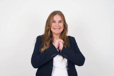 Tatlı yüzlü, çekici, orta yaşlı bir kadın. Ellerini yüzünün yanında çapraz tutuyor. Hoş bir şey için heyecanlanıyor..