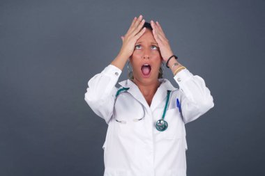 Korkunç, stres, şok. Gri arka planda izole edilmiş, elleri birbirine kenetlenmiş genç, duygusal deli kadın portresi. İnsani duygular, yüz ifadesi kavramı.