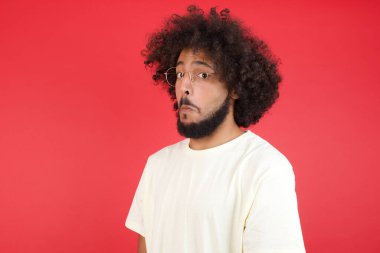 Afro saçlı genç adamın kırmızı duvara karşı kafası karışık. 