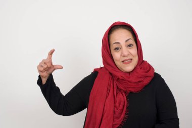 İzole edilmiş arka planda küçük boy ve ölçü sembolü gösteren el kol hareketi yapan bir kadın. Kameraya bakıp gülümsüyor. Ölçme konsepti. Stüdyoda poz veren başörtüsü takan orta yaşlı bir Arap kadın.