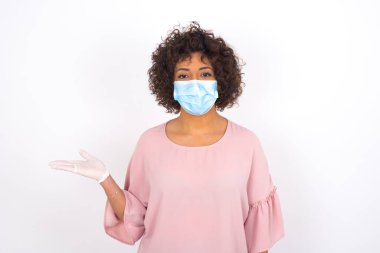 Yüz maskesi takan ve elini beyaz stüdyo arka planında gösteren bir kadın.
