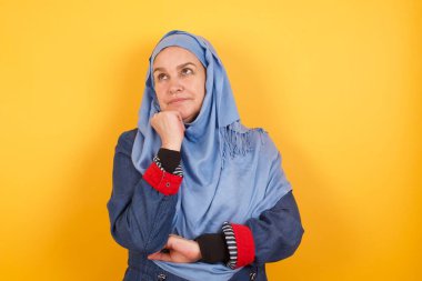 Yüz ifadeleri ve duygular. Düşünceli, orta yaşlı, tesettürlü Müslüman kadın başının altında el ele tutuşmuş, şüpheli bir bakış atıyor..