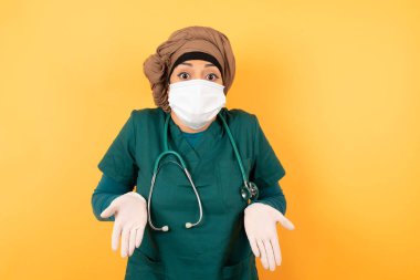 Kafası karışmış, maske takmış, kolları açık, omuzlarını silkip: 