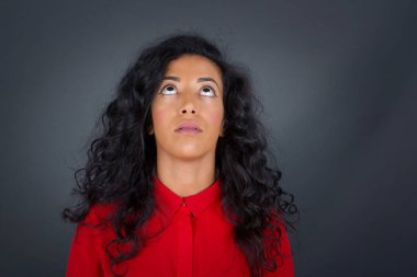 Kıvırcık saçlı, kırmızı tişörtlü gizemli esmer kadının esrarengiz gülümsemesiyle yukarı bakan portresi. Güzel gülümseyen kız, gri duvara bakıyor.. 