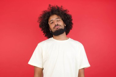 Kızıl duvara karşı poz veren afro saçlı genç adam.   