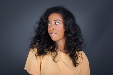 Düşünceli, genç bir kadın, bakışlarını kaçırıyor, dudaklarını ısırıyor gri duvara karşı hoş bir poz düşünüyor..