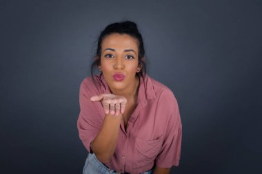 Sevimli bir kadın kameraya yumruk atar, sevgilisine aşkını gösterir ya da uzaktan veda eder, gri stüdyo arka planında izole bir şekilde..