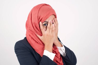 Endişe - güzel Müslüman bir kadının kavramsal bir görüntüsü siyah ceket giyer ve elleriyle yüzünü örterek parmaklarının arasından dışarı bakar. Bir şeyden ya da birinden korktun mu?.