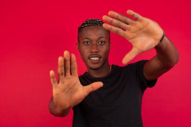El hareketli parmak çerçevesi. Stüdyo duvarına yaslanırken kameraya bakıp el kol hareketi yapan yakışıklı Afro-Amerikan bir adamın portresi..