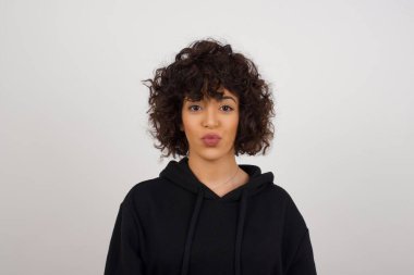 Çekici, açık renk saçlı kadın dudaklarını yuvarlıyor, günlük kıyafetler giyiyor, doğrudan kameraya bakıyor, memnuniyetini ifade ediyor, gri arka planda soyutlanıyor. İnsanlar, vücut dili kavramı.