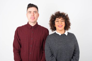  Mutlu ve komik yüzlü, gülen ve dil gösteren sıradan kıyafetler giyen çift. Günlük giysiler giyip stüdyonun arka planında dikiliyor..