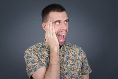 Şaşkınlık - adam heyecanla yüzüne bakıyor. Heyecandan yana bakan mutlu genç adam şaşırdı. Gri arka planda beyaz erkek model.