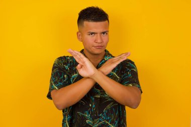 İzole bir arka planda duran, günlük kıyafetler giyen genç, yakışıklı İspanyol bir adam. Reddedilme ifadesi olumsuz işaret göndererek el ele tutuşuyor mu?.