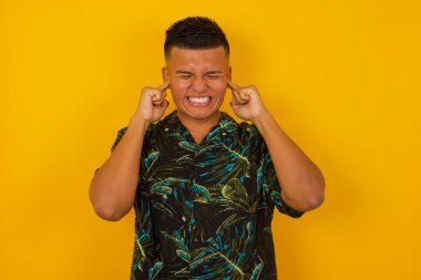 Bu sinir bozucu sesi çıkarmayı kes! Mutsuz genç İspanyol erkeğin vesikalık fotoğrafı endişeli yüz ifadeleri takınıyor, parmaklarıyla kulaklarını tıkıyor, üst katındaki komşulardan gelen gürültüden rahatsız oluyor..