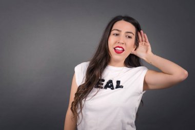 Gri arka planda duran güzel bir kadın bir şeyler dinliyor.. 