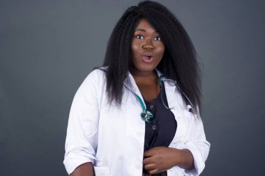 Şok olmuş bir şekilde kameraya bakan, hayret ve şaşkınlık içinde bağıran, şaşırmış, şaşırmış Afrikalı-Amerikalı kadın doktorun vesikalık fotoğrafı.