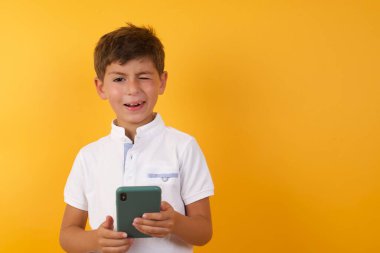 Akıllı telefonlu şirin çocuk sarı duvara göz kırpıyor.  