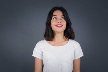 Düz saçlı, esrarengiz bir gülümsemeyle yukarı bakan gizemli büyüleyici kadının portresi. Güzel gülümseyen kız, gri duvara bakıyor..