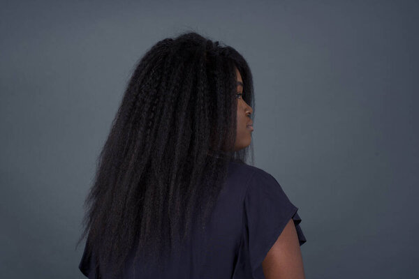 The back side view of African American woman standing against gray wall. Studio Shoot.
