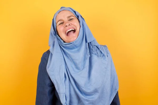 ジハブで楽しい中年イスラム教徒の女性は楽しいと良いジョークや歌を笑い 壁に立ってカジュアルな服を着ています — ストック写真