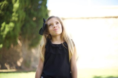 Kasvetli, merak eden genç bir kız dudaklarıyla yukarıya bakıyor, önemli bir şey hakkında üzülürken, ellerini aşağıda tutuyor..