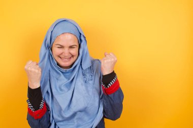 Güçlü, başarılı, orta yaşlı, tesettürlü, tesettürlü, yumruklarını sıkan, sevinç ve heyecanla haykıran Müslüman kadının portresi. Zafer, başarı ve başarı kavramı.