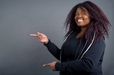 Gündelik giysiler içinde, ağzı açık, neşeli ve şaşkın bir ifadeyle pozitif çekici, Afro-Amerikalı kadın içeride inanılmaz bir şey gösteriyor. Reklam kavramı.