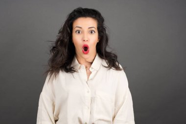 Gayri resmi giyinmiş güzel esmer kadının kafası karışmış. Gri arkaplanda duruyor.  