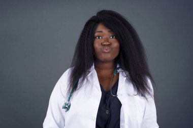 Hoş görünümlü genç Afrikalı Amerikalı kadın doktor, dudaklarını öpecek gibi tutuyor, mutlu bir ifadesi var, suratını buruşturmuş.. 