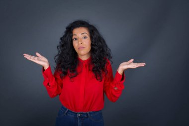 Şaşırmış ve budala esmer, kıvırcık saçlı, kolları açık kırmızı tişörtlü, omuzlarını silkeleyen, 