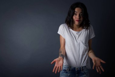 Kafası karışmış, kolları açık genç bir kadın omuzlarını silkip 