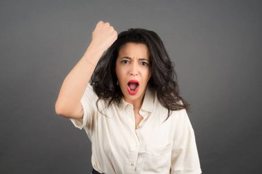 Güzel esmer kadın bağırıyor. Gri arkaplanda duruyor. 