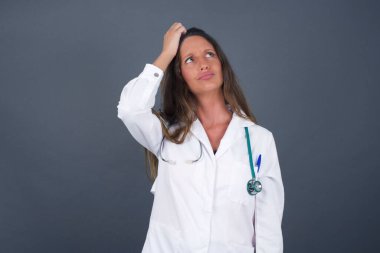 Tüh, ne yaptım ben? Güzel doktor kadın korkmuş ve pişmanlık dolu bir ifadeyle el ele tutuşuyor. Gri arka planda dikilen günlük giysiler giyiyor..