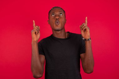 Yakışıklı Afro-Amerikan erkek portresi izole edilmiş arka planda şaşkın şaşkın bakıyor ve parmaklarıyla garip bir şey gösteriyordu..