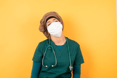 Yeşil üniformalı, genç, güzel, Müslüman bir doktor stüdyo duvarında dikilmiş, boş gününün keyfini çıkarıyor..