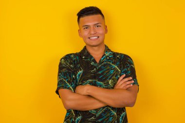 Genç yakışıklı adamın portresi mutlu gülümsüyor ve kollarını kavuşturup kameraya bakıyor. Pozitif ve kendinden emin kişi.