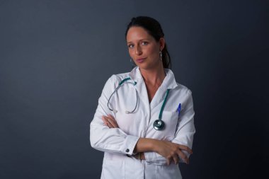 Gri arka planda izole edilmiş güzel, kendine güveni yüksek genç bir doktor kadın. Geniş bir gülüşü var, kollarını kavuşturuyor. Meslektaşıyla tanıştığına memnun, şık giyinmiş..