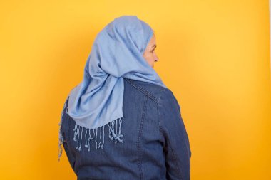 Orta yaşlı, tesettürlü Müslüman bir kadının duvarın önünde duruşu. Stüdyo Çekimi.