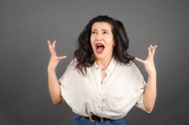 Güzel esmer kadın bağırıyor. Gri arkaplanda duruyor. 