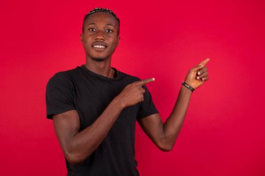 Reklam konsepti. Olumlu, güzel, kafiyeli Amerikalı arka planda gülümseyen adam işaret parmaklarıyla işaret ediyor ve boş fotokopi alanına bakıyor..