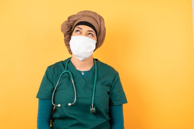 Hüzünlü, yeşil tıp üniformalı, üzgün, tıbbi üniforma giyen ve ellerini aşağıda tutan genç ve güzel Müslüman bir kadın..