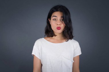 Çekici, açık renk saçlı, yuvarlak dudaklı, doğrudan kameraya bakan, tatminini ifade eden, gri arka planda izole edilmiş bir kadın. İnsanlar, vücut dili kavramı 