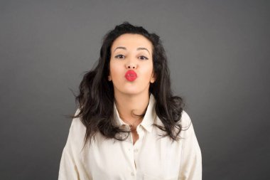 Gri arka planda gelişigüzel giyinmiş güzel esmer kadın öpüşüyor..  