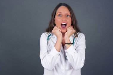 Mutlu bir doktor kadının stüdyo fotoğrafı. Morali yüksek olduğu için el ele tutuşuyor. Ertesi gün için arkadaş fikrini seviyor, gri duvarda izole edilmiş. Pozitif duygular.