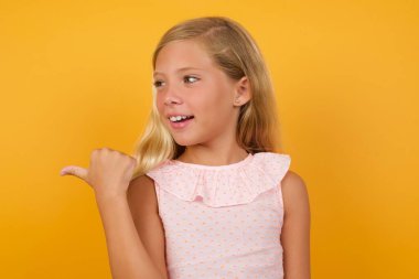 Stüdyonun sarı arka planına dayanan sevimli sarışın küçük kız.  