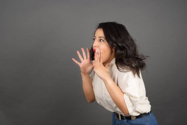 Gayri resmi giyinmiş güzel esmer kadın korkuyor. Gri arkaplanda duruyor. 