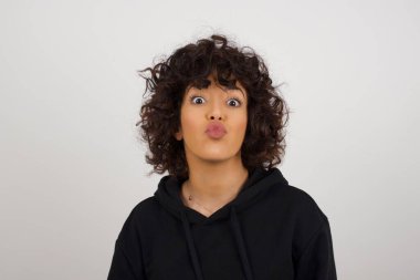 Kapüşonlu hoş görünümlü genç bir kadın birini öpecekmiş gibi dudaklarını tutuyor, mutlu bir ifadesi var, asık suratlı. Dışarıda dikiliyorum. Güzellik konsepti.