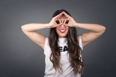 Güzel bir kadın gözlük jesti yapıyor. Gri arkaplanda duruyor. 