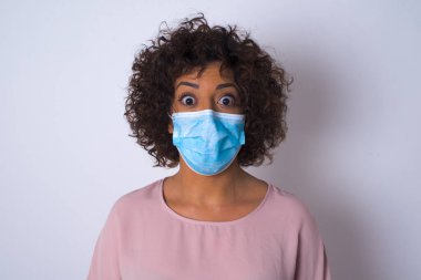 Yüz maskesi takan ve beyaz stüdyo arka planında izole edilmiş günlük kıyafetler giyen bir kadın.