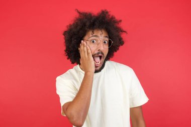 Afro saçlı genç adam kırmızı duvara karşı şaşırdı. 